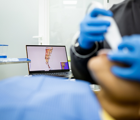 Dentist taking digital impression in foreground with image of teeth on computer in background