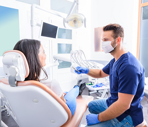 Dentist with mask sitting next to patient in dental chair