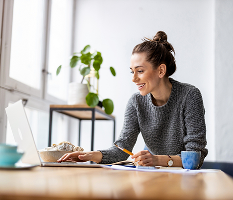 Woman with sweater holding pencil and typing on laptop