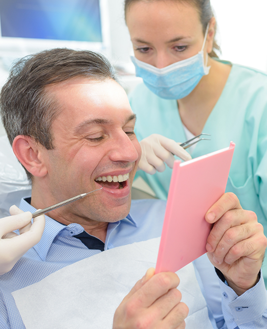 Male dental patient checking smile in mirror with dentist next to him