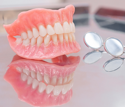 Full dentures on reflective surface next to dental mirror