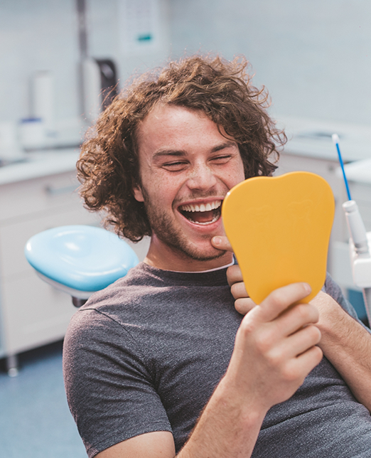 Man in dental chair checking smile in mirror