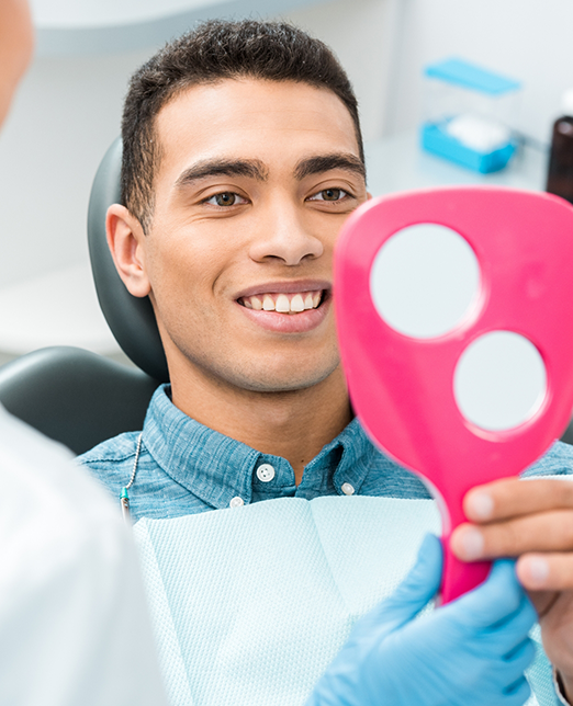 Smiling male dental patient looking at handheld mirror