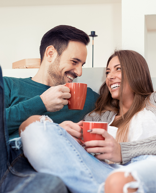 Man and woman with coffee mugs sitting on couch